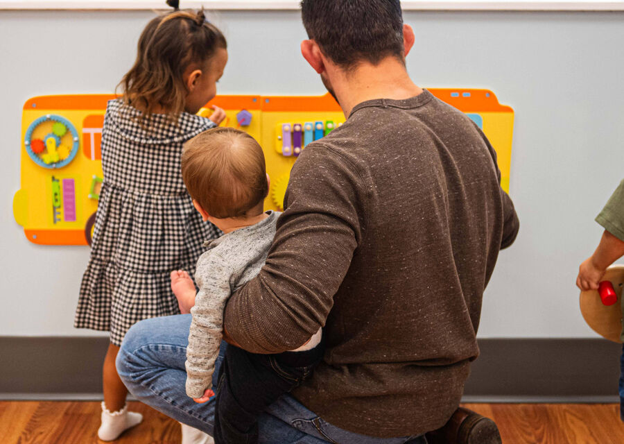 A parent and three children playing at a wall activity board